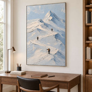 Small climbers following ridges across snowy mountains in a silver frame, displayed in a home office.