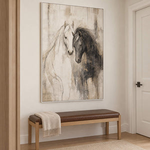 A white horse and a dark horse leaning close on an ivory ground in a white frame, displayed in a hallway.