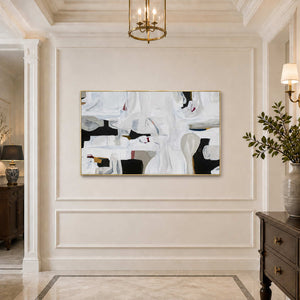 Gold framed white and charcoal abstract artwork on a softly illuminated paneled hallway wall.