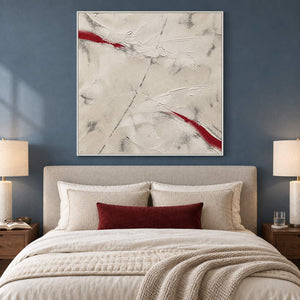 Ivory textured abstract painting with red diagonal strokes in a white frame in a bedroom.