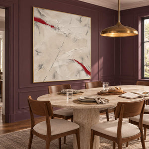 Ivory textured abstract painting with red diagonal strokes in a gold frame in a dining room.