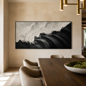 Black framed coastal painting with textured white crests beside a warm dining table.