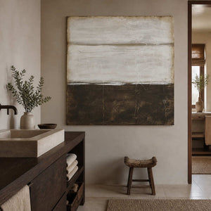 Frameless earth-toned abstract beside a rectangular stone bathroom basin and woven wooden stool.