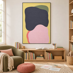 Yellow abstract painting with charcoal, blush, olive, and coral shapes in a black frame in a children's reading room.