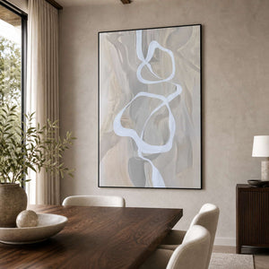 Black framed ribbon abstract artwork beside a wooden dining table and upholstered cream chairs.