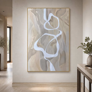 Gold framed white ribbon artwork above a pale wooden floor in a quiet hallway.