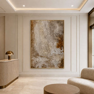 Gold framed warm neutral abstract artwork beside seating in a refined hotel lobby.