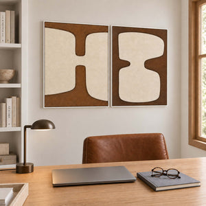 Two panels of complementary ivory organic forms on brown grounds in white frames, displayed in a home office.