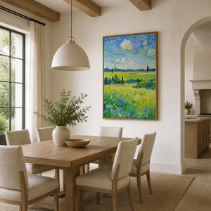 Meadow landscape in a wood frame beside a wooden dining table and cream chairs.