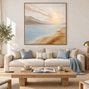 Coastal painting with pale blue water, golden sand, and distant hills in a brown wood frame in a living room.