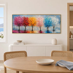 A row of colorful trees reflected beneath a pale sky in a gold frame, displayed above a dining table.