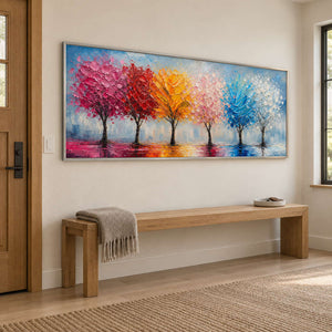 A row of colorful trees reflected beneath a pale sky in a silver frame, displayed above an entryway console.