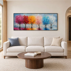 A row of colorful trees reflected beneath a pale sky in a black frame, displayed above a sofa in a living room.