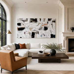 Frameless white and black abstract artwork above a long cream sofa beside a fireplace.