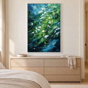 Artwork showing small white flowers among diagonal layers of green and deep blue strokes in a bedroom above a low dresser, with a white frame.