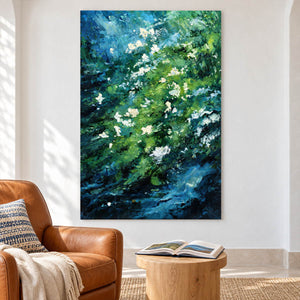 Beside a reading chair, an artwork with no outer frame shows small white flowers among diagonal layers of green and deep blue strokes.