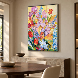 Artwork showing purple flowers, red cup-shaped blooms and blue-white sprays on yellow in a dining area beside the table, with a black frame.