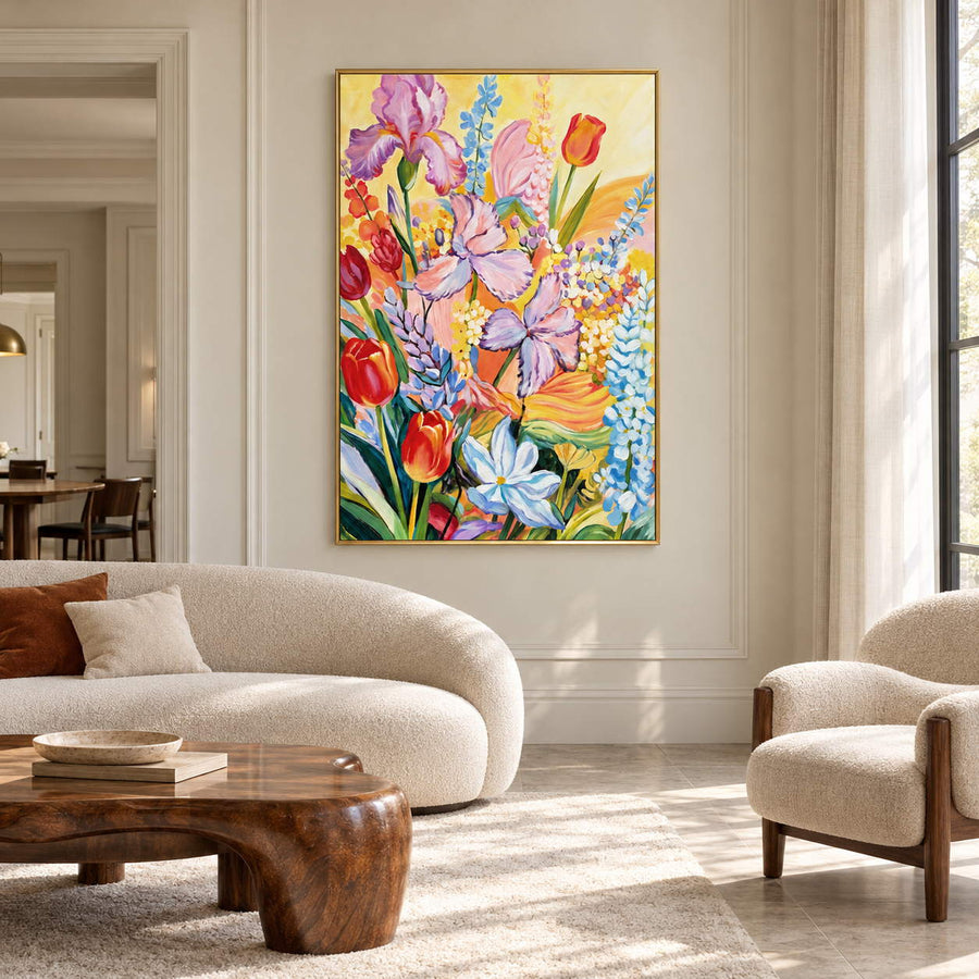 Purple flowers, red cup-shaped blooms and blue-white sprays on yellow in an artwork with a gold-colored frame, displayed in a living room above seating.
