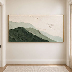 Layered dark and pale green mountains beneath an ivory sky in a gold frame, displayed in a hallway.