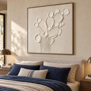 Sculptural warm white petals and leaves raised from a monochrome canvas, displayed in a bedroom in a brown wood frame.