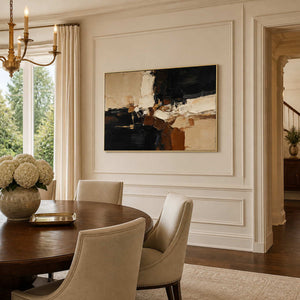 Gold framed black and cream abstract artwork beside a round wooden dining table.