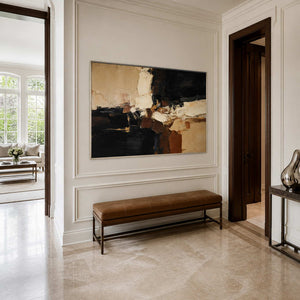 Silver framed horizontal abstract artwork above a leather bench in a paneled entryway.