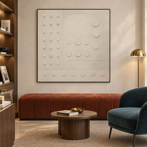Warm white textured wall art with raised circles and quiet geometry, displayed in a lounge in a black frame.