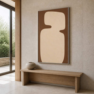 Silver framed warm brown abstract artwork above a wood bench in a stone entryway.
