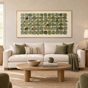 Keeping a Little Spring in a gold frame above a cream sofa with sage cushions and an oval light wood table.