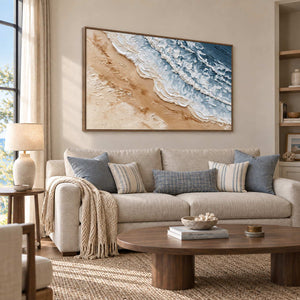 Kissing the Shore in a wood frame above a cream sofa with blue and striped cushions.