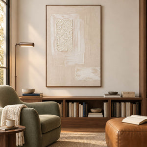 Ivory and blush relief painting with layered rectangles and a rough central panel in a brown wood frame in a reading room.