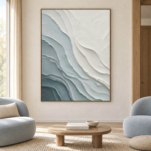 Layered blue-gray and chalk-white coastal relief painting in a brown wood frame in a living room.