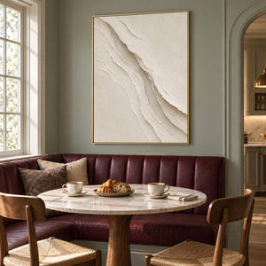 Hand-painted ivory abstract wall art with layered cream palette-knife relief, displayed in a dining room in a gold frame.