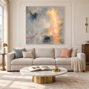 Blue-gray abstract painting with gold, blush, and dark blue marks in a white frame in a living room.