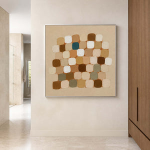 Silver framed neutral square painting beside pale stone shower walls and wooden cabinets.