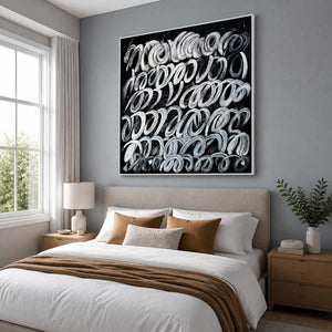 White framed black and white abstract painting above a light upholstered bed.
