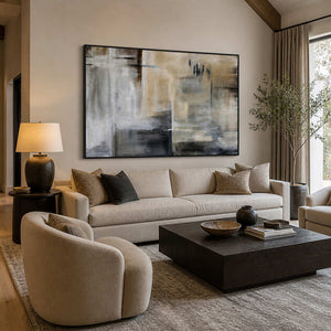 Black framed gray and sandy abstract painting above a cream living room sofa.