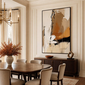 Black framed warm abstract artwork above a sideboard beside a wooden dining table.