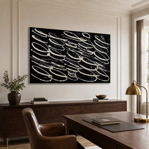 Silver framed black and white abstract loops above a wooden office sideboard.