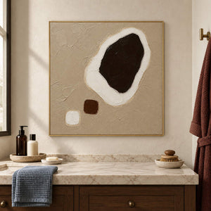 Taupe abstract painting with a large dark brown shape edged in white and two small forms in a gold frame beside a bathroom vanity.