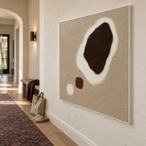 Taupe abstract painting with a large dark brown shape edged in white and two small forms in a white frame in a hallway.