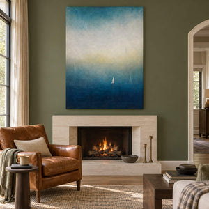 Atmospheric coastal painting with a white sail drifting across deep teal water, displayed beside or above a fireplace without an outer frame.