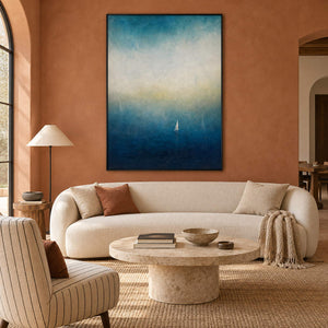 Atmospheric coastal painting with a white sail drifting across deep teal water, displayed in a living room in a black frame.