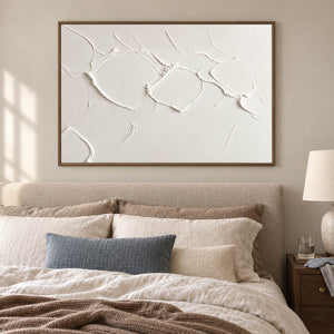 Chalk-white abstract relief painting with raised irregular seams in a brown wood frame in a bedroom.