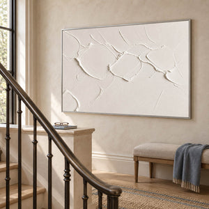 Chalk-white abstract relief painting with raised irregular seams in a silver frame on a stair landing.