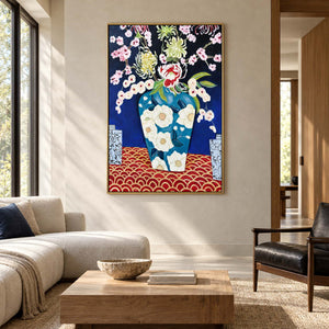 Flowers in a blue floral-patterned vase above a red surface with repeated gold-colored arcs in an artwork with a gold-colored frame, displayed in a living room above seating.