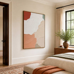 Wood-framed peach and white abstract artwork beside a bed with green and rust textiles.
