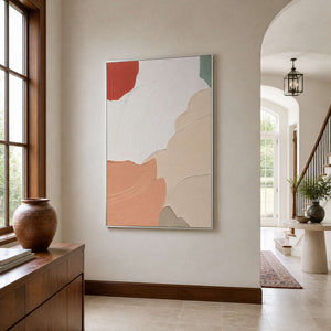 Silver-framed peach and white abstract artwork beside an arched entryway and wooden stair rail.