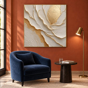 Hand-painted sculptural flower in layered ivory, white, and warm gold, displayed in a hotel lounge in a gold frame.