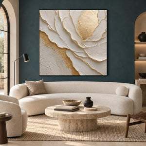 Hand-painted sculptural flower in layered ivory, white, and warm gold, displayed in a living room in a black frame.